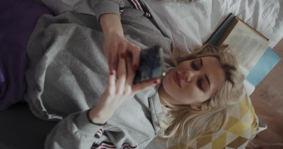 A woman is laying down and texting on her cellphone
