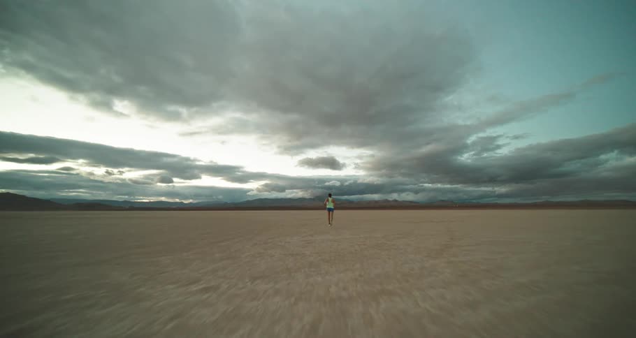 Man wearing sports clothes jogging on the flat plains of a desert at evening
