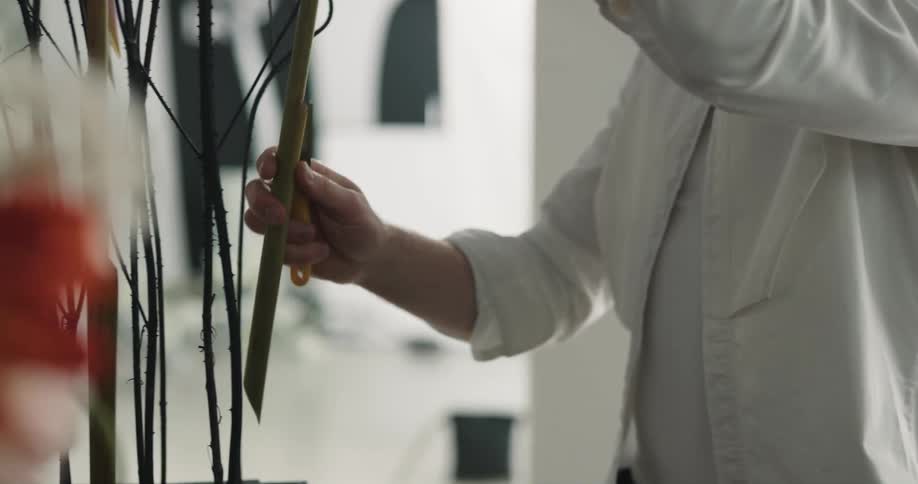 Man cuts the stem of a flower using a knife on a flower shop