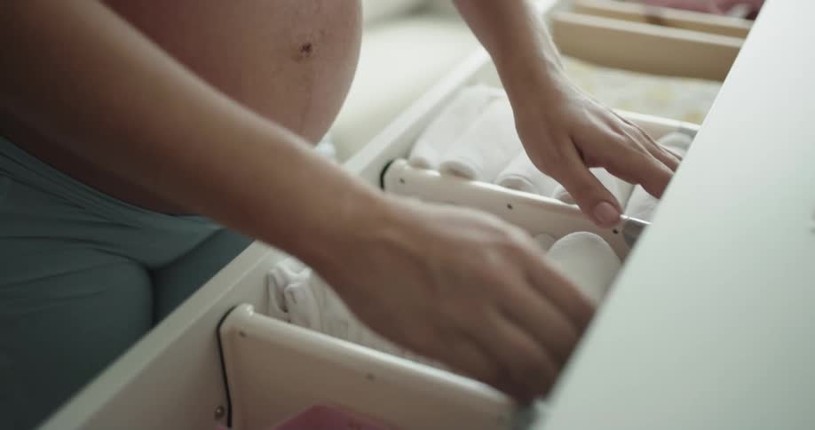 A pregnant woman arranges fabric in a drawer during the day