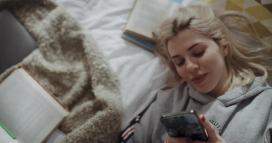 Young woman is laying on bed browsing through her phone