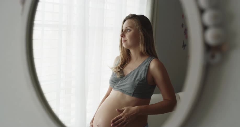 Young pregnant woman is rubbing belly in the mirror