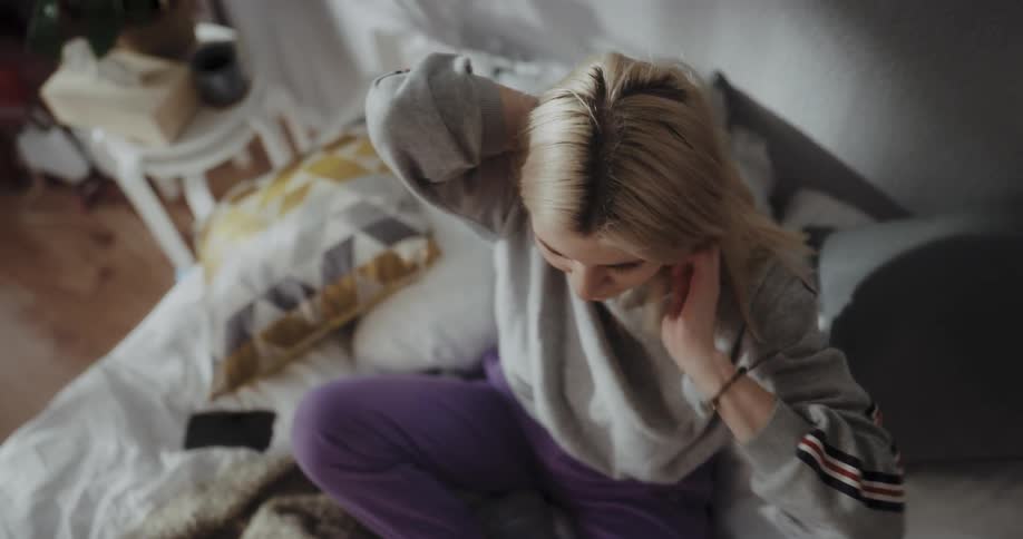 Blonde woman with gray sweater and purple pants types on laptop and lies on bed resting