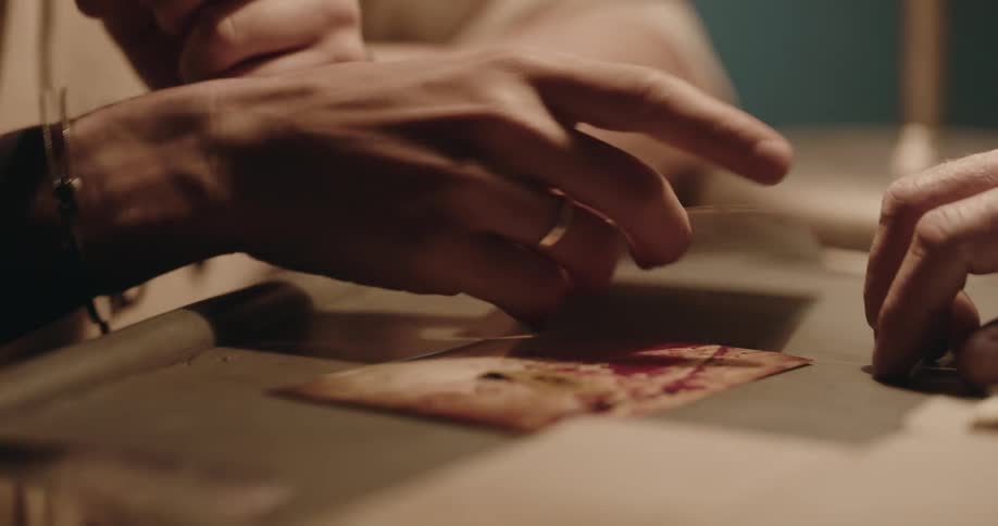 A folder opens and a hand pushes photographs over to another person who picks up the photos with his handcuffed hands