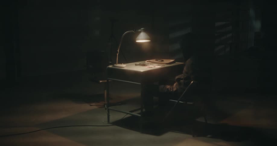A man is sitting in a chair at a table in a dark room