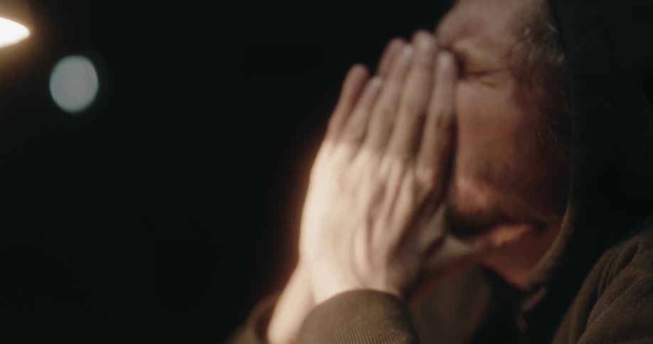 A man rubs his face in the dark room