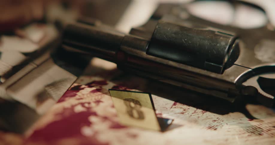 Shadow and light play over revolver lying on surface stained with blood