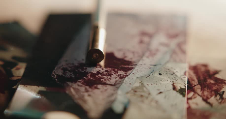 Bullet casing resting over a photograph covered in blood over a desk