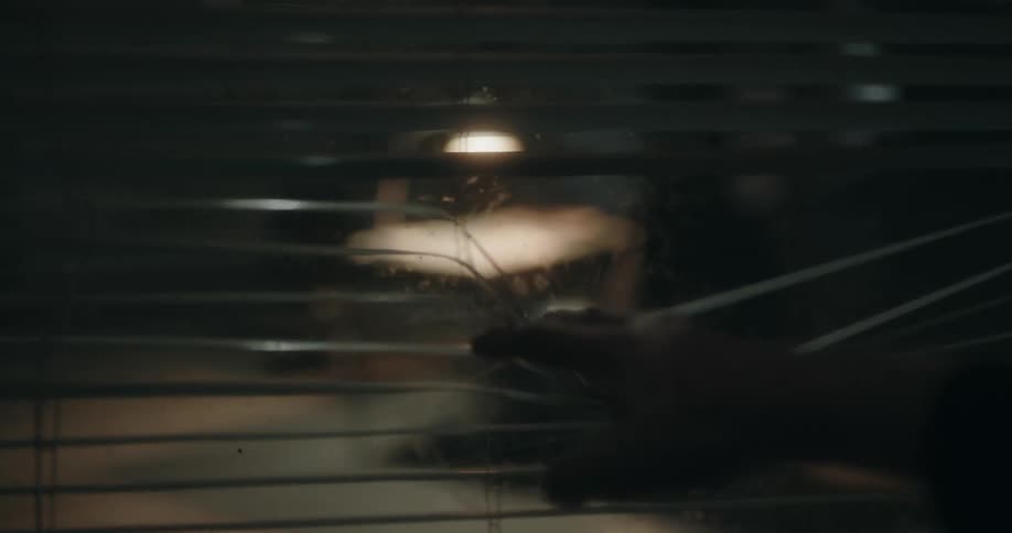 Man looks through a window into an interrogation room where a man is sitting on a chair