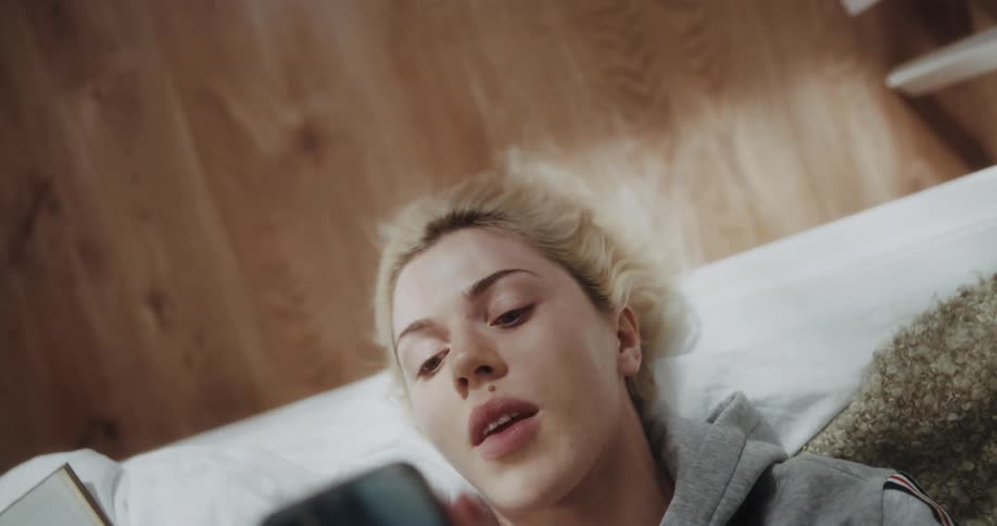 A woman uses her smartphone while lying in bed during the day
