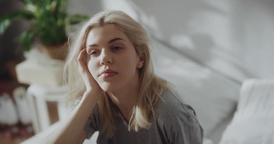 A young woman yawns and rubs her face as she sits up in bed