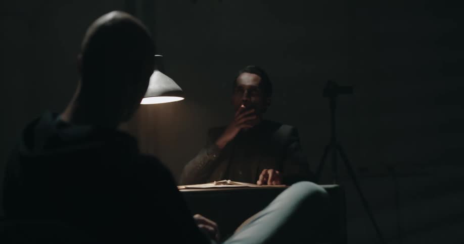 A man angrily slams papers around on a desk as he smokes a cigarette
