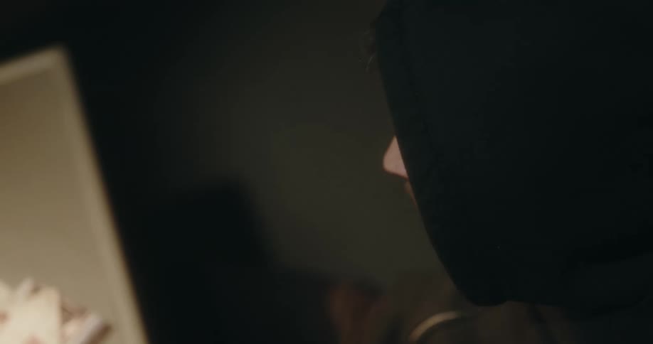 Man wearing hoodies sits in at table in dim room