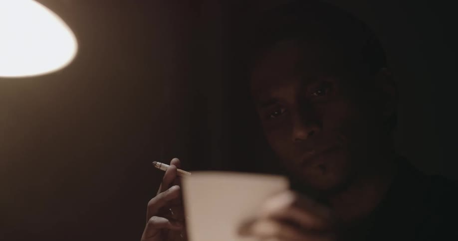 A man smokes a cigarette while looking at photos in a dark room