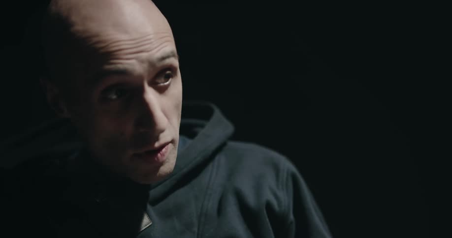 Nervous man answers questions inside a dimly lit interrogation room