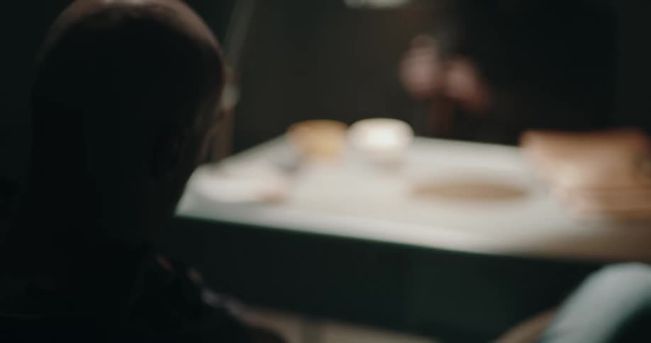 Man wearing a hoodie leisurely sitting inside an interrogation room greets a detective