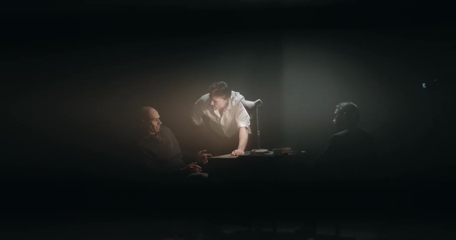 Cop on his feet in interrogation room strikes table while he and his partner interrogate a suspect