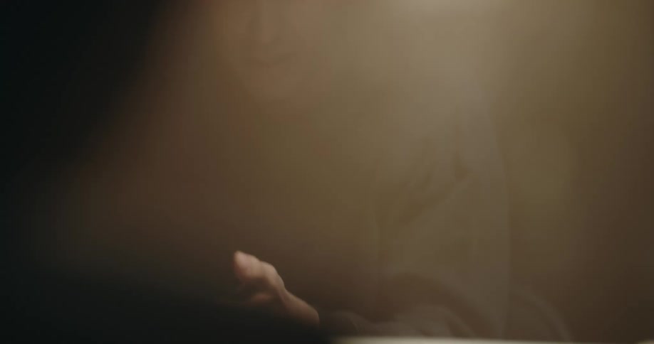 A man shines a bright light over the face of a suspect being interrogated