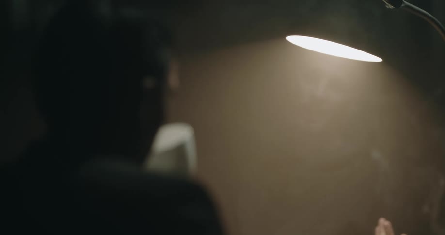 Silhouette of a detective smoking while listening to a man detained on an interrogation room
