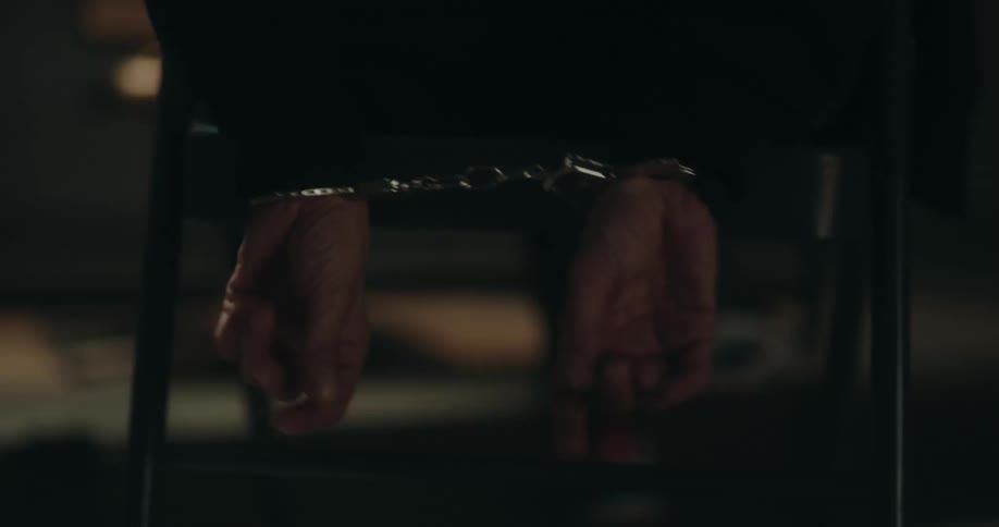Man sitting on an interrogation room struggles with handcuffs