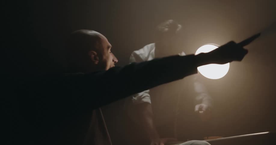 Detective aggressively interrogates a suspect under a bright light inside an interrogation room