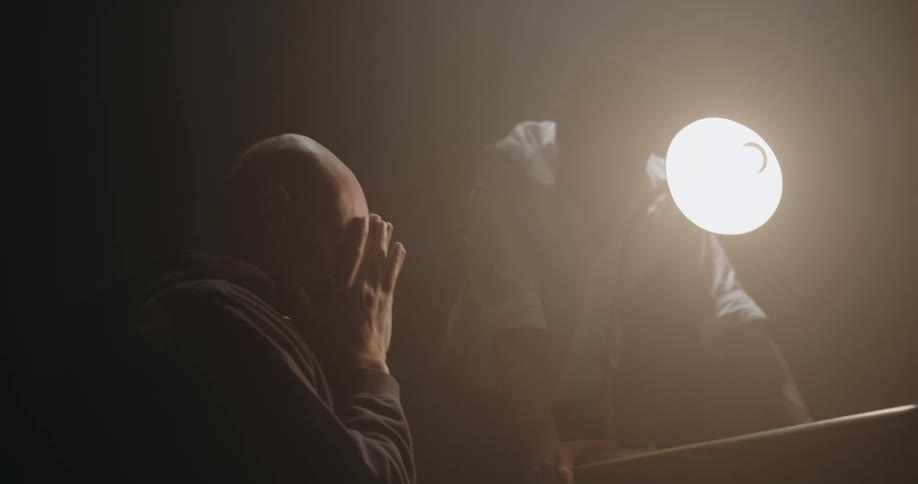 Man aggressively interrogates suspect sitting on a chair inside an interrogation room