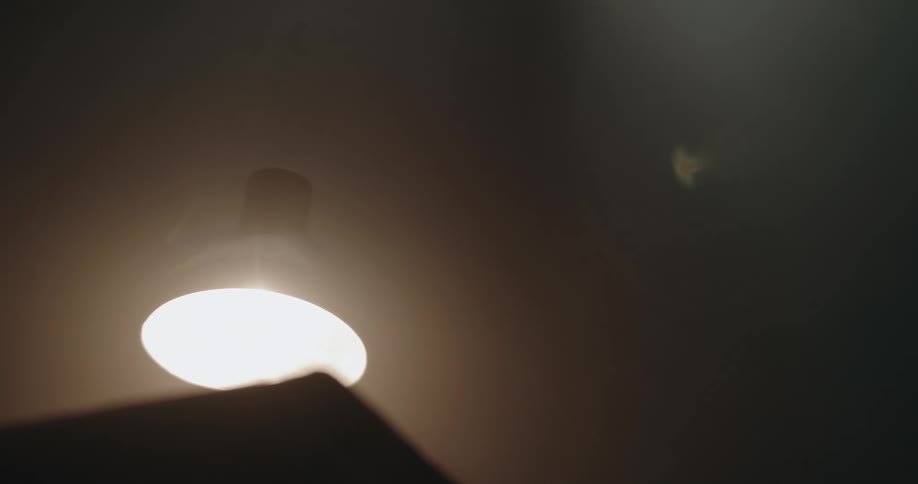 Smoke floats over lamp on table in dim room as ceiling fan casts a rotating shadow