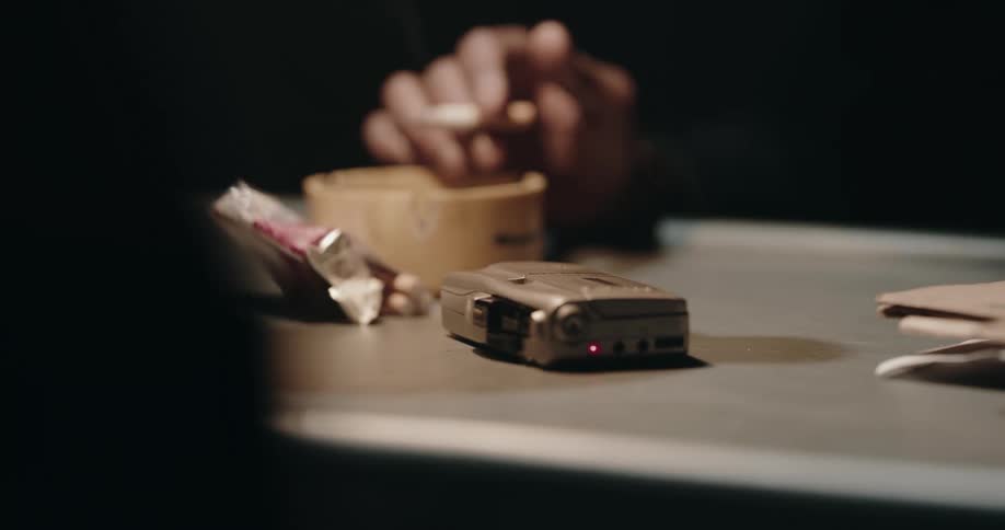 Suspect talks to a detective inside a dimly lit interrogation room in front of a tape recorder