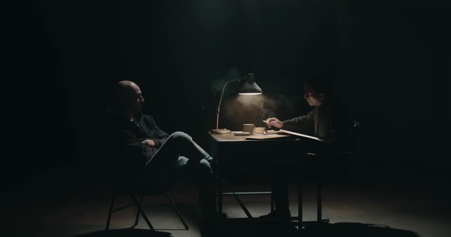 Two men are talking together indoors in a dark room