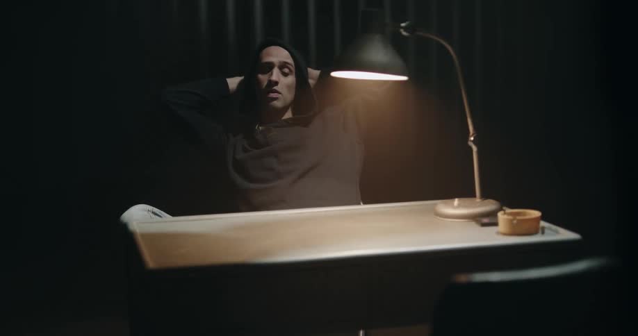 Man leisurely sitting on a chair in front of a desk inside an interrogation room