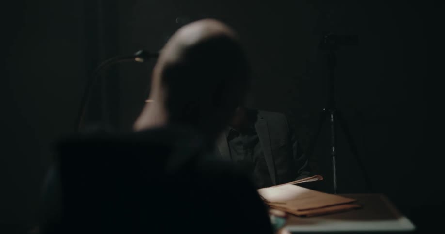 Detective aggressively shakes pictures in front of a suspect inside an interrogation room