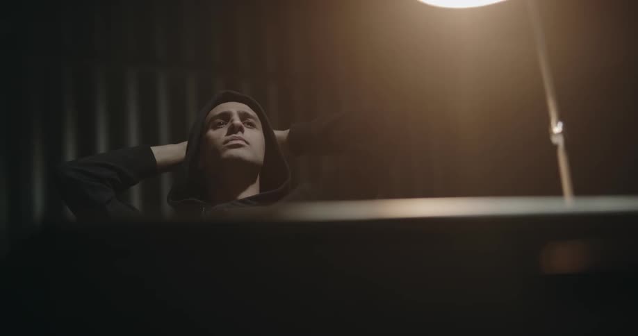 Man wearing a hoodie waits leisurely inside an interrogation room