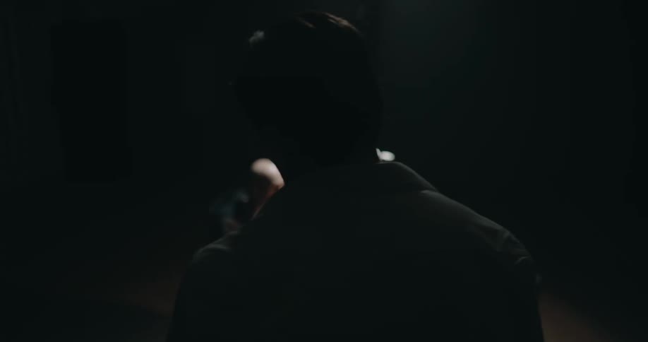 Man stands in interview room observing as an officer questions another man