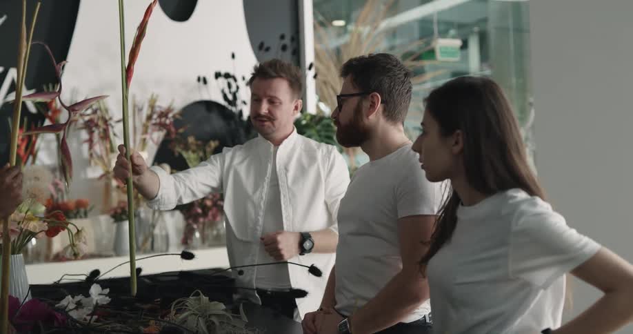 Male florists discusses large flower stalk with two people standing in shop