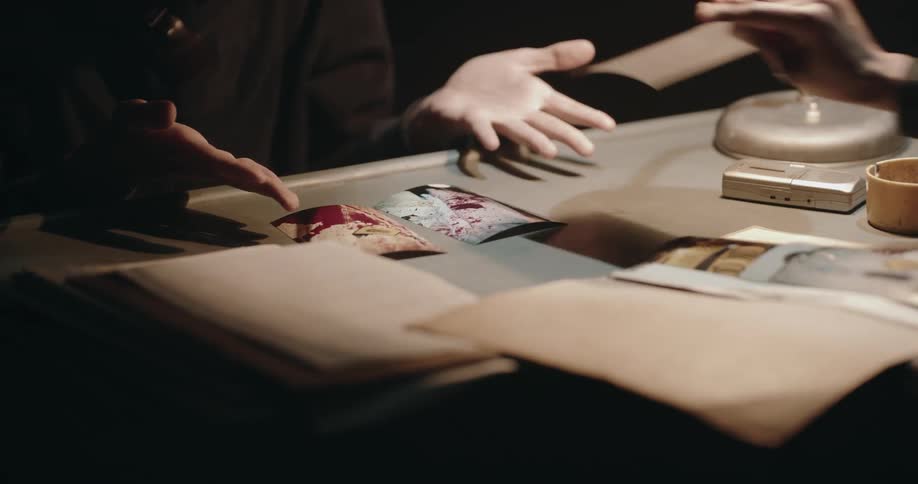 An interrogator opens a file and angrily places photographs in front of a prisoner demanding answers