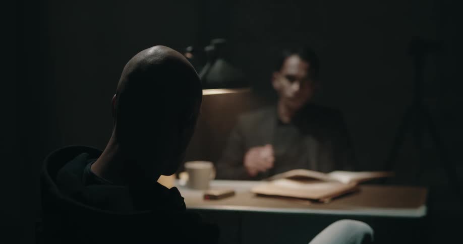 Detective questioning a suspect inside a dimly lit interrogation room
