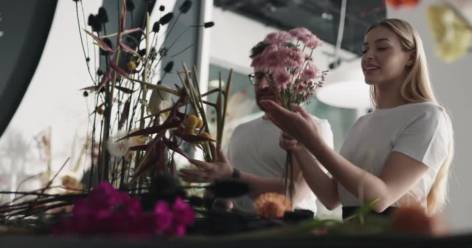 A man brings more flowers over to a woman who is trimming and arranging