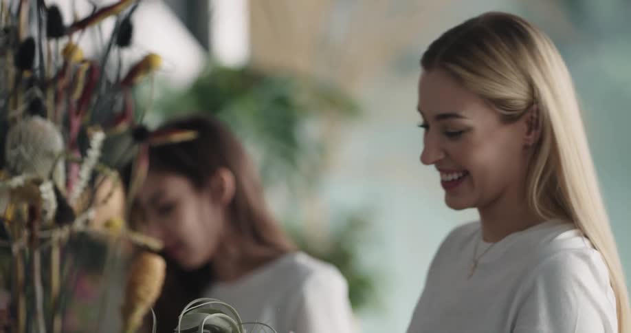 Woman hands plant to another and then helps her place it in floral arrangement