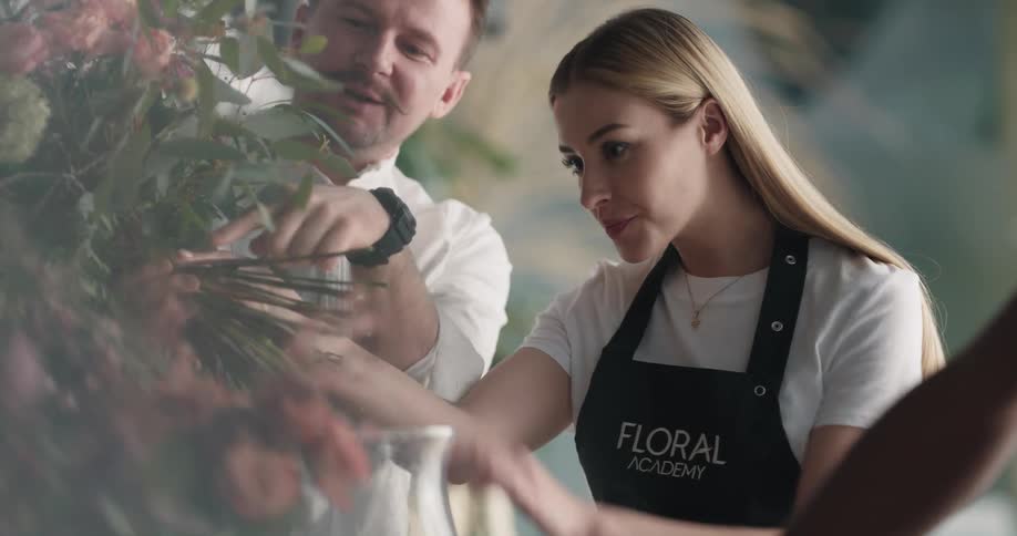 A woman examines a flower arrangement while speaking to a pair of her coworkers