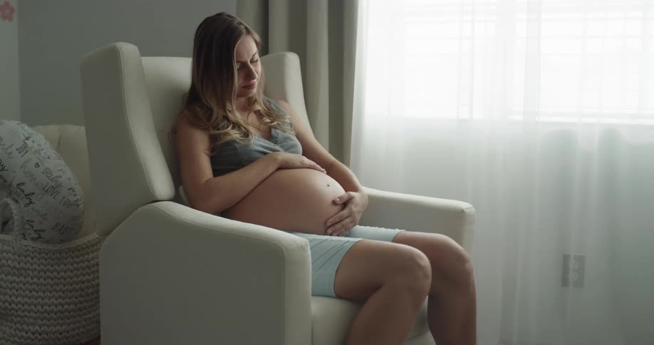 A woman is sitting and rocking in a chair while rubbing her pregnant belly