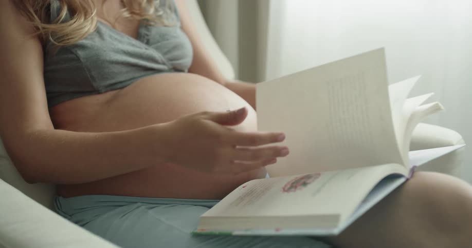 A pregnant woman is reading a book at home