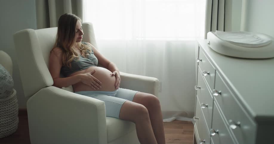 A pregnant woman is sitting in her room on a chair