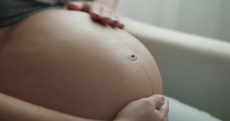 Pregnant woman strokes her belly sitting on couch