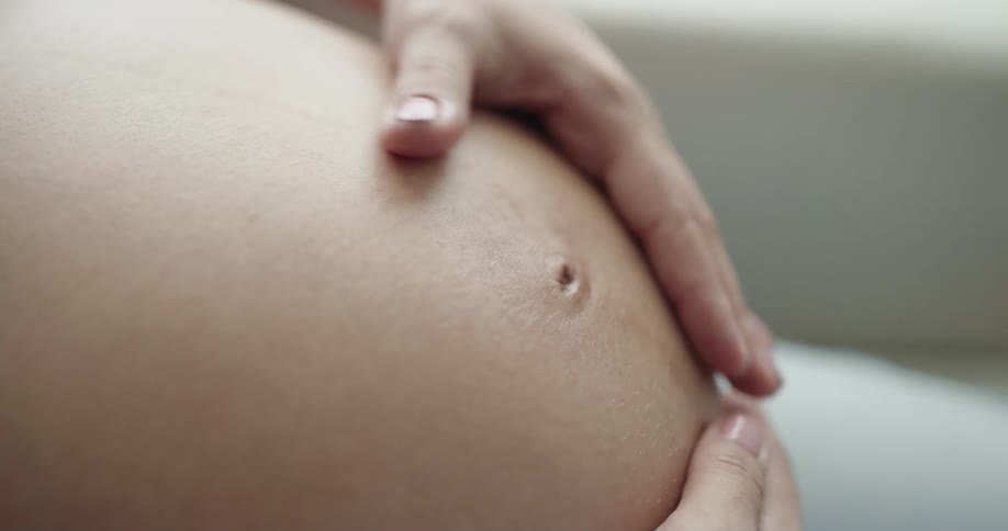 Pregnant mother gently rubs and massages her belly with both hands