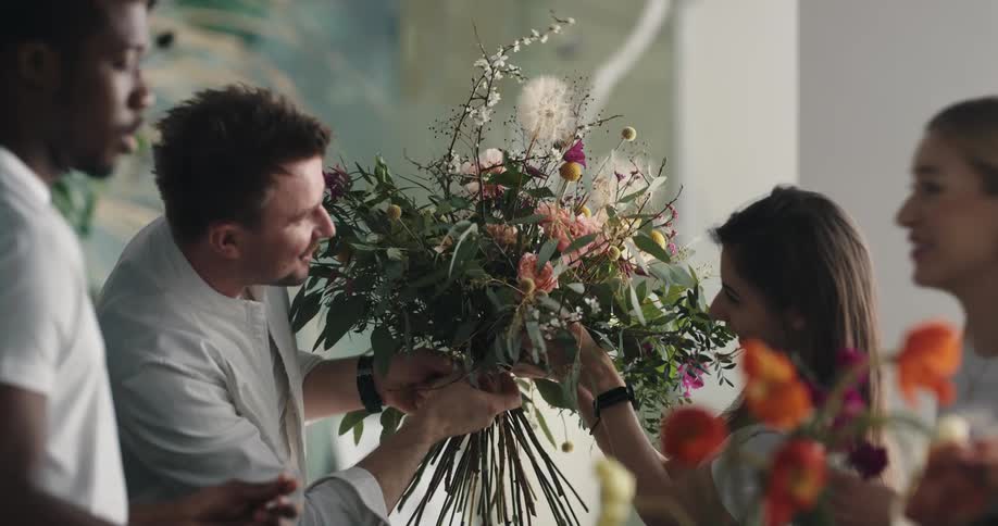A group of people prepare a flower arrangement together indoors during the day