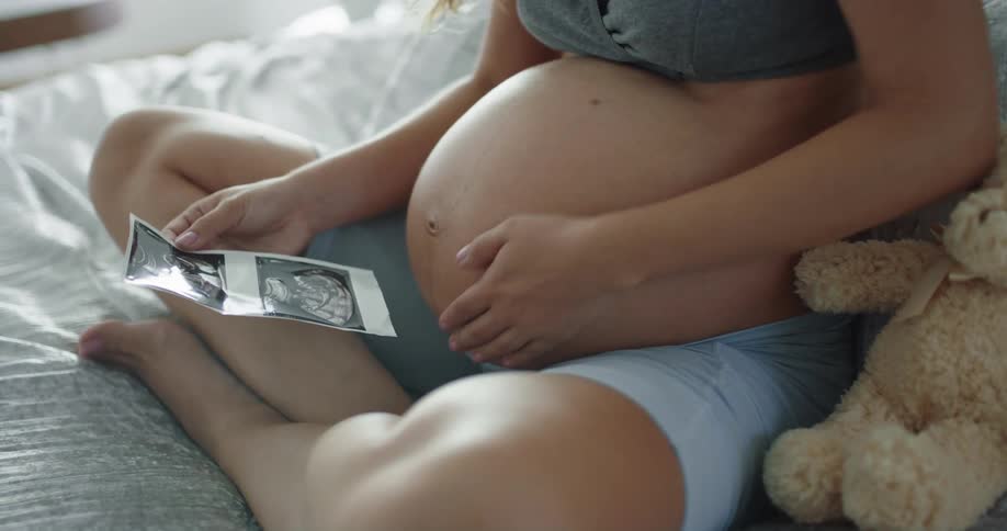 Pregnant mother looking at an ultrasound gently rubs and massages her belly with both hands