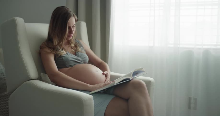 Young pregnant woman is reading a book