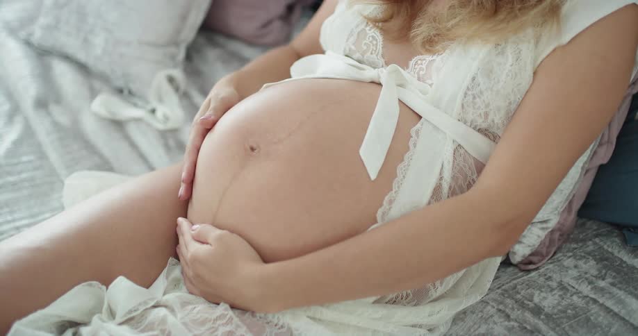 Female wearing lingerie relaxing on bed caressing her large pregnant belly