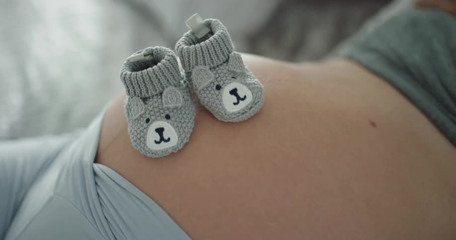 Baby boots resting over the belly of a pregnant woman moving with the baby kicks