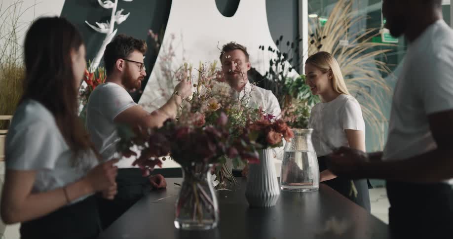 Boss of a flower shop teaches employees how o assemble a flower bouquet